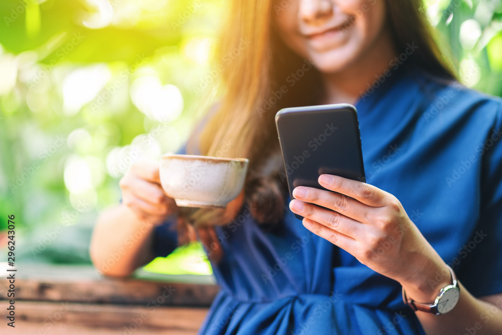 Closeup image of a beautiful asian woman holding and using mobile phone while drinking coffee in the garden Closeup image of a beautiful asian woman holding and using mobile phone while drinking coffee in the garden