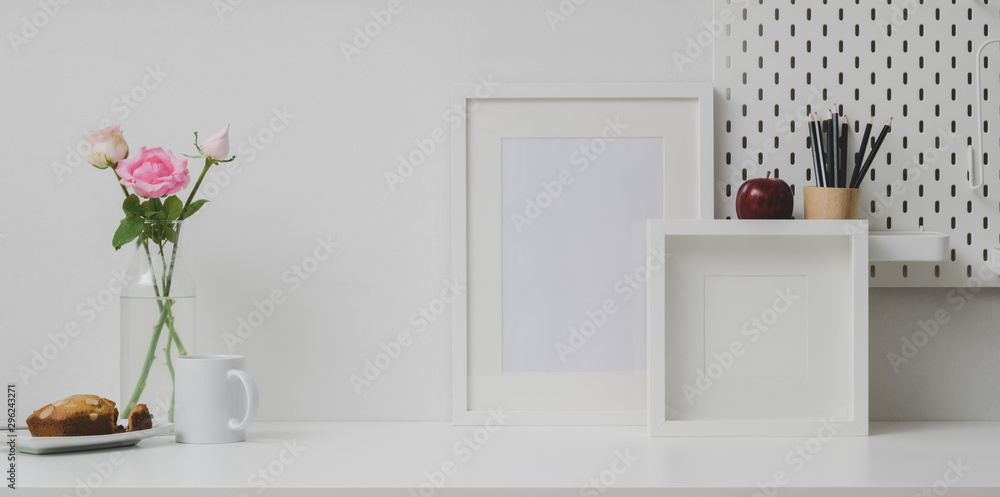 Fototapeta premium Comfortable workplace with mock up frame and copy space on white table and white wall