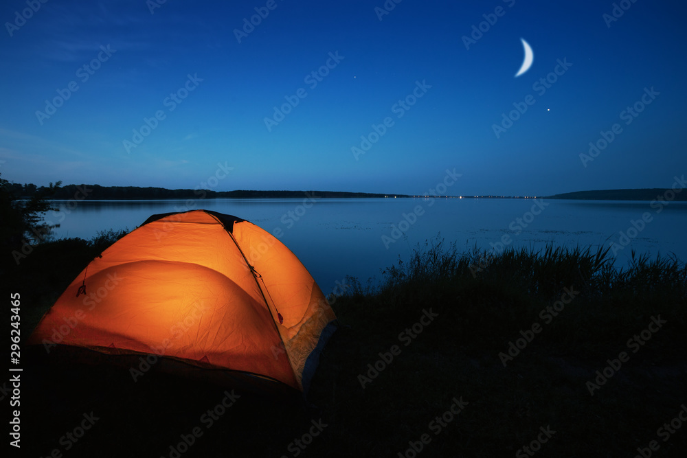 Orange tourist tent lit by a lake