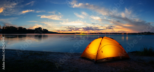 Canvas Print Orange tourist lit tent by the lake at sunset