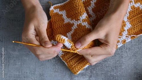 adult girls hands crochet hook with orange and white cotton threads on stone tabletop background, view from above close-up full HD stock video footage in realtime