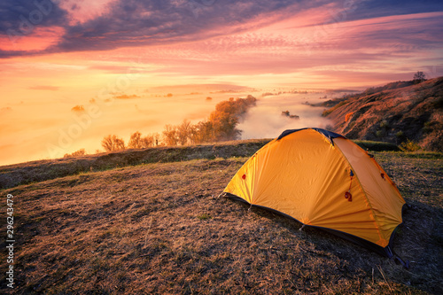 Orange tourist tent on hill above foggy river