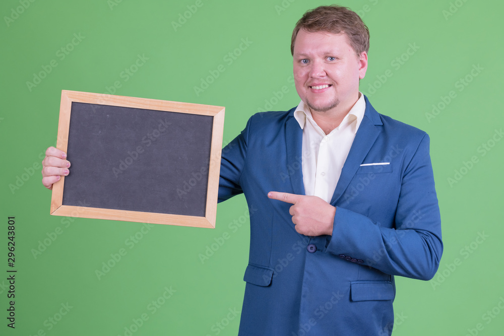 Portrait of happy overweight bearded businessman holding and pointing at blackboard Portrait of happy overweight bearded businessman holding and pointing at blackboard