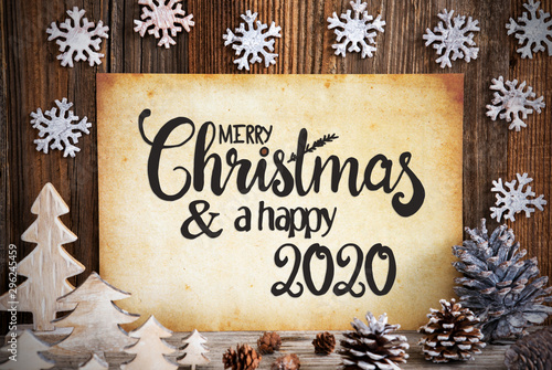 Old Paper With English Text Merry Christmas And Happy 2020. Christmas Decoration Like Tree, Fir Cone And Snowflakes. Brown Wooden Background