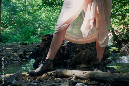 The legs of a young girl in a light summer dress and vintage shoes standing by a small stream on a clear sunny day in the forest. Through the thin dress the sun's rays shine © Александр Коновалов
