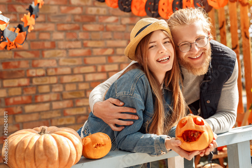 Young adult man and woman hugging, holding halloween pumpkin in hands
