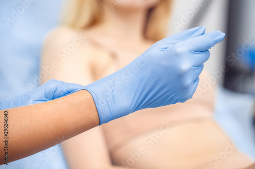 Cosmetology Service. Young woman at beauty clinic sitting blurred doctor close-up putting on gloves © Viktoriia