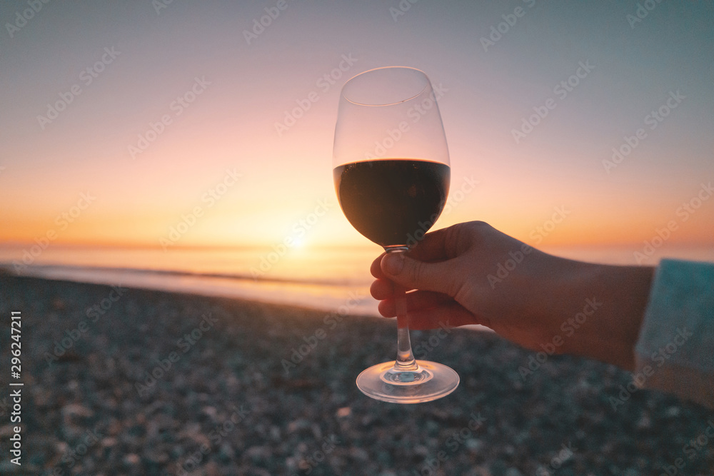 Person drinking glass of red wine during watching sunset and enjoying sea vacation