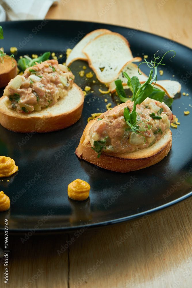 Salmon tartare on fried croutons served on a stylish black plate. Restaurant Food. Wooden bakcground. Close up Salmon tartare on fried croutons served on a stylish black plate. Restaurant Food. Wooden bakcground. Close up