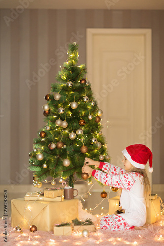 Cute blonde girl 5 years old decorating Christmas tree. Bedroom decorated with Christmas garlands. home interior, Xmas celebrate, happy new year 2020 concept