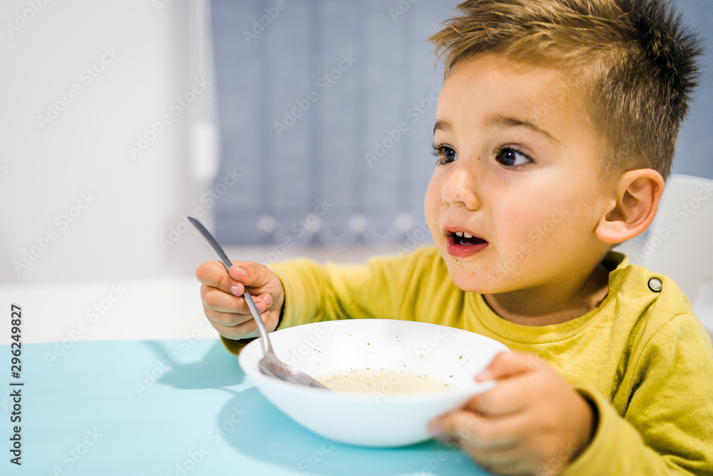 Portrait of small boy child eating soup meal or breakfast having lunch by the table at home with spoon white kindergarten Portrait of small boy child eating soup meal or breakfast having lunch by the table at home with spoon white kindergarten