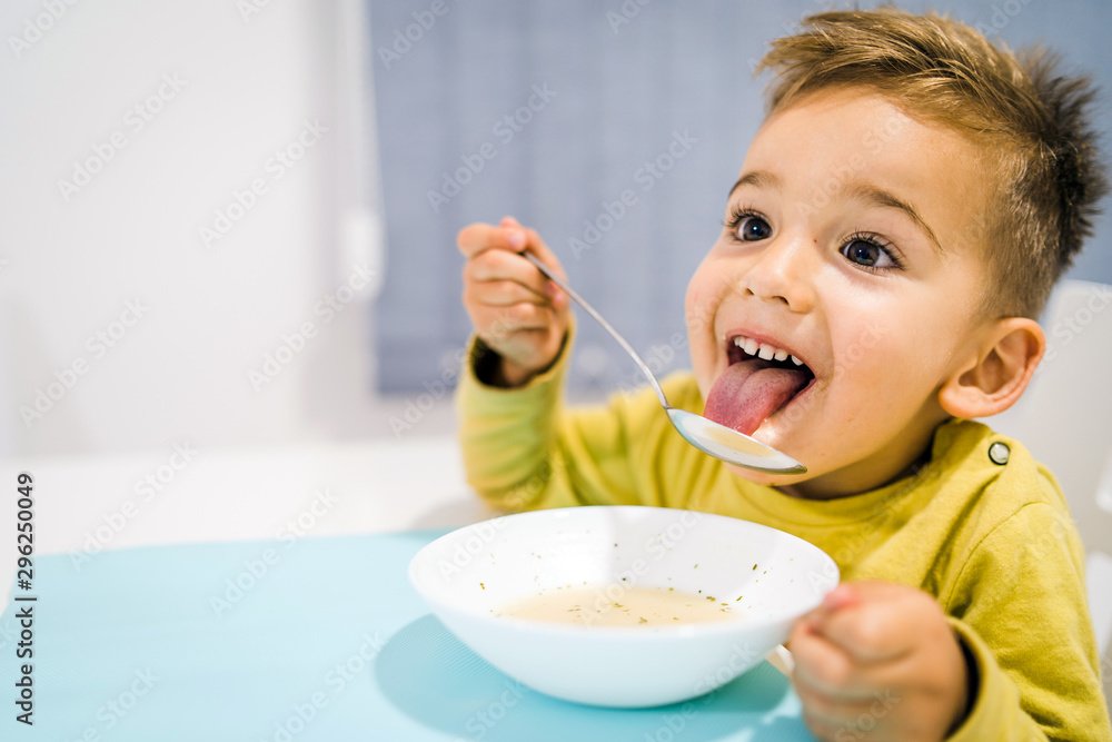 Portrait of small boy child eating soup meal or breakfast having lunch by the table at home with spoon white kindergarten Portrait of small boy child eating soup meal or breakfast having lunch by the table at home with spoon white kindergarten