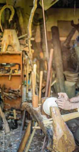 Hand carving a wooden bowl with a foot powered wood lathe, in an old carpenter's workshop with carpenter's wood tools in background, in rural Ariege, France photo