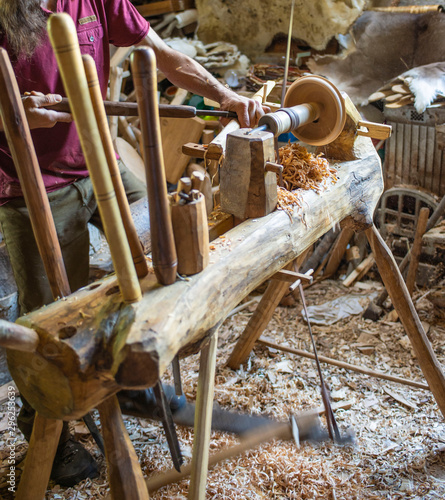 Hand carving a wooden bowl with a foot powered wood lathe, in an old carpenter's workshop with wood shavings and sawdust in background. Rural Ariege, France