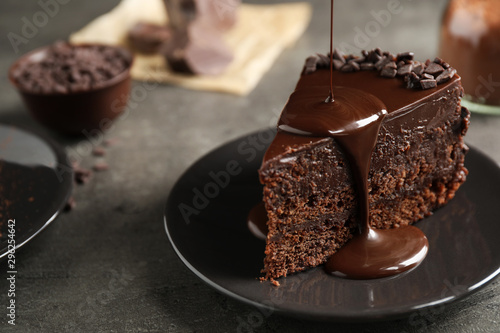 Fotobehang Pouring chocolate sauce onto delicious fresh cake on grey table, closeup