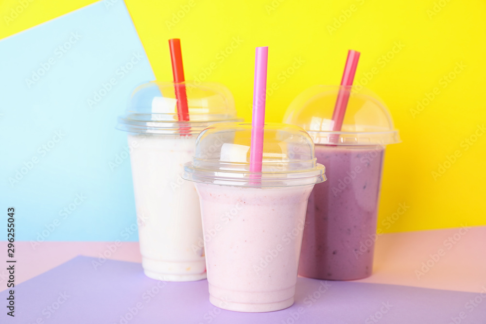 Different tasty milk shakes in plastic cups on color background Different tasty milk shakes in plastic cups on color background