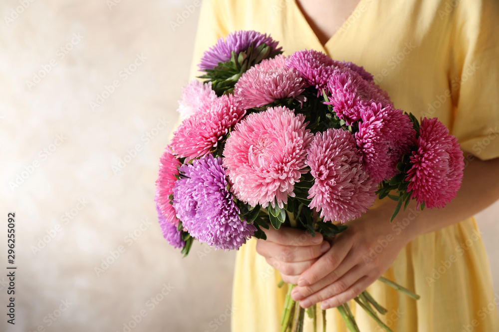 Woman holding bouquet of beautiful aster flowers on beige background, closeup. Space for text