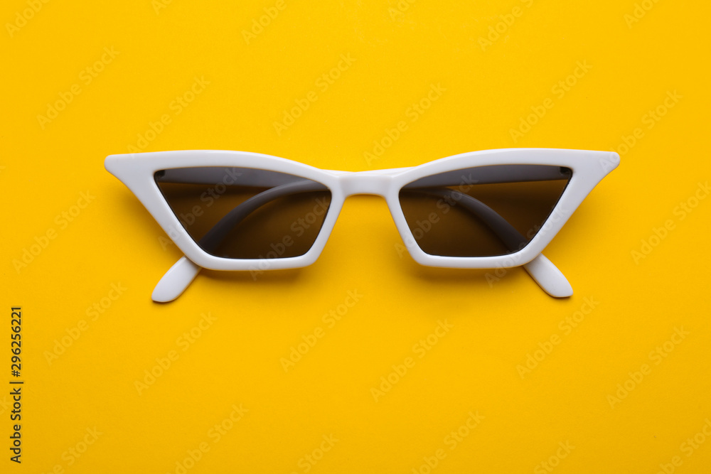 Stylish sunglasses on yellow background, top view. Fashionable accessory