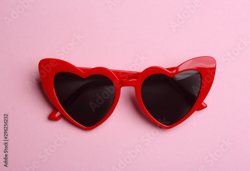 Stylish heart shaped sunglasses on pink background, top view. Fashionable accessory