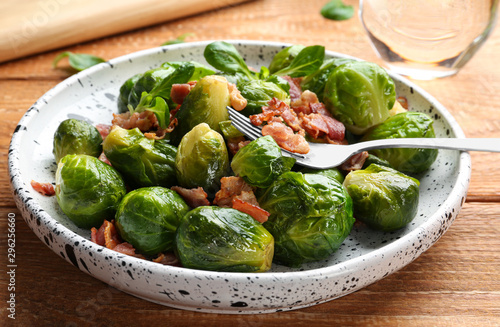 Tasty roasted Brussels sprouts with bacon on wooden table, closeup