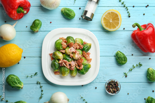 Flat lay composition of tasty roasted Brussels sprouts with bacon on light blue wooden table