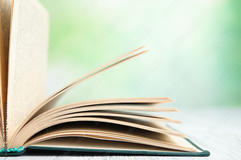 Naklejka premium Open book on white wooden table against blurred green background, closeup