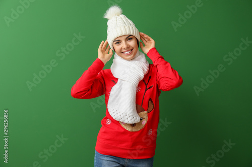 Young woman in Christmas sweater, hat and scarf on color background