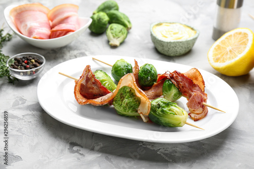Skewers with Brussels sprouts and bacon in plate on grey table