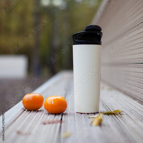 Billede på lærred Plastic thermo Cup with hot drink and tangerines on a bench in the autumn Park