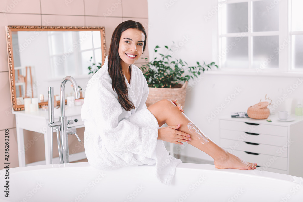 Beautiful young woman applying cream on her legs in bathroom Beautiful young woman applying cream on her legs in bathroom