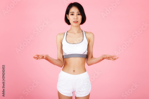 Young slim fitness asian woman in white sportwear shows something on her palms isolated on pink background. © skarie
