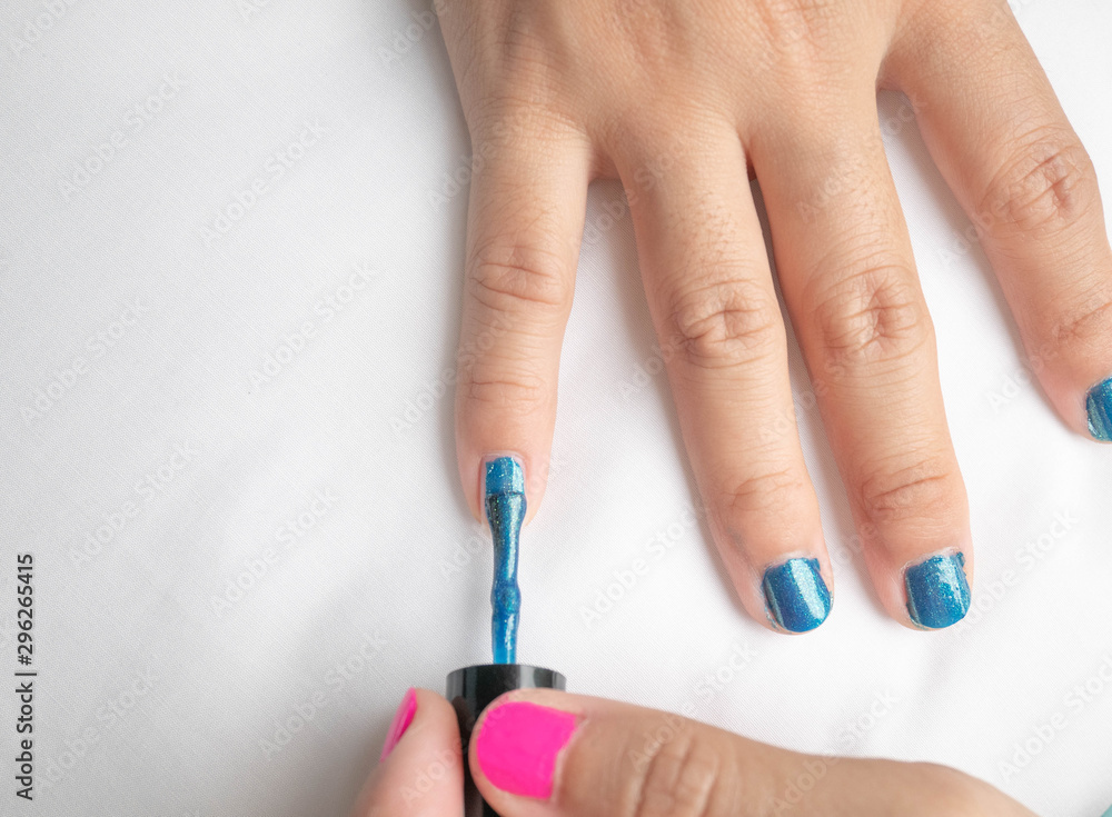 Close-up of female hands painting blue nail varnish, self made manicure at home. Close-up of female hands painting blue nail varnish, self made manicure at home.