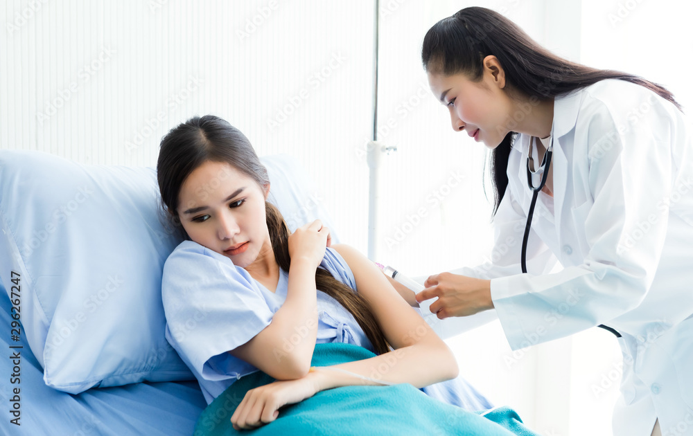 Asian young female doctor with syringe to the arm of Asian young female patient on Bed for better healing In the room hospital background. Asian young female doctor with syringe to the arm of Asian young female patient on Bed for better healing In the room hospital background.
