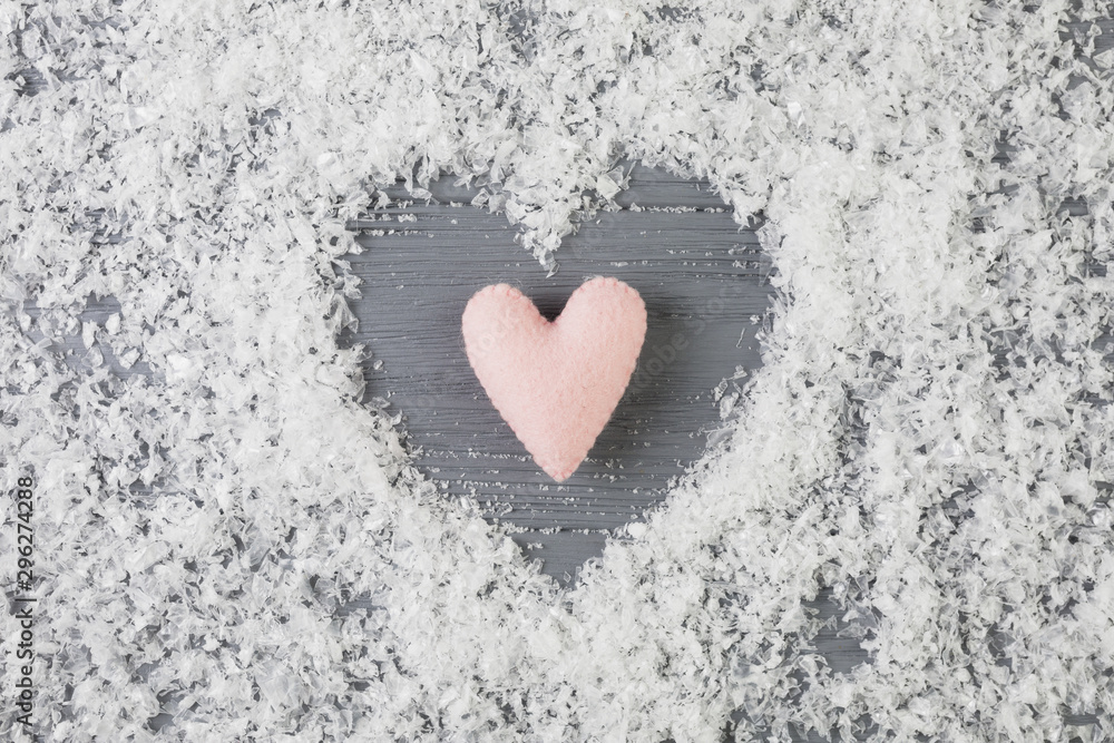 Pink heart between decorative snow on wooden desk