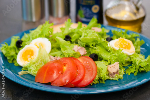 Salad with tuna, eggs, tomato, olives, spices and croutons, sauce or oil on blue plate