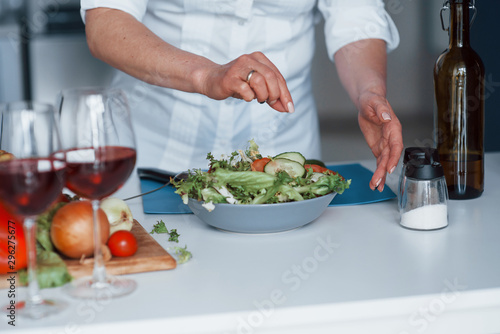 Woman in white shirt preparing food on the kitchen using vegetables