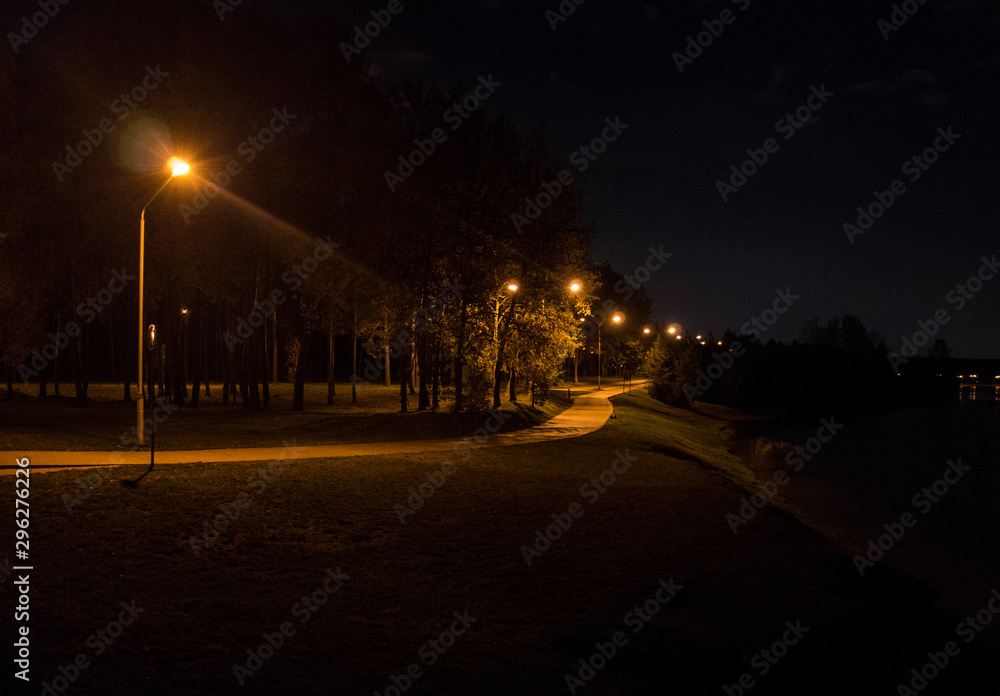 Night park with luminous lanterns. Contrasting yellow light.