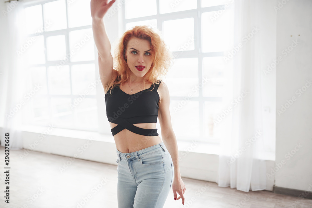 Active female dancer. Attractive redhead woman posing in the spacey room near the window