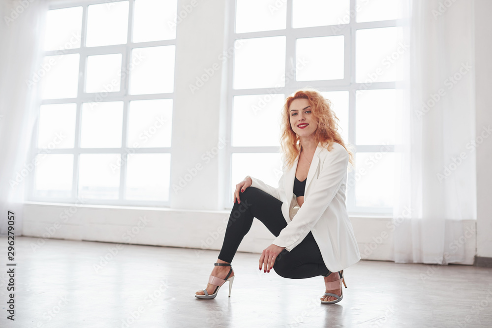 Sitting on the floor. Attractive redhead woman posing in the spacey room near the window Sitting on the floor. Attractive redhead woman posing in the spacey room near the window