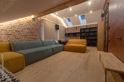 Obraz na plátně Soft couch and empty bookcase located inside spacious living room with brick wal