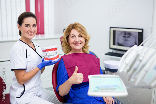 attractive female doctor holding artificial jaws and cheerful mature woman patient thumbs up