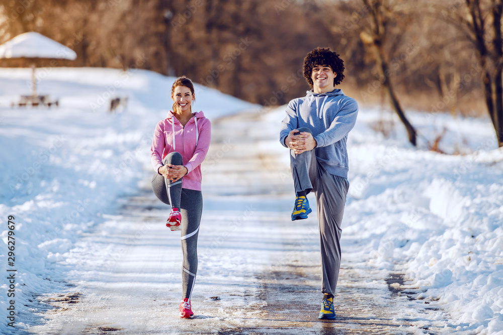 Φωτογραφία Cheerful cute caucasian couple in sportswear stretching legs on country road and looking at camera