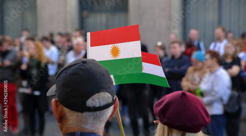 Two flags of Kurds hold by adult woman and men, standing on their back, during street protest against Turkish invasion in Syria, in background other protesters in soft focus photo