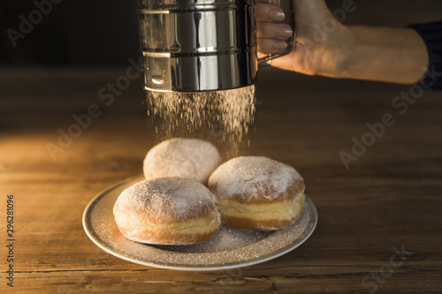 Crop hand spilling powdered sugar on doughnuts
