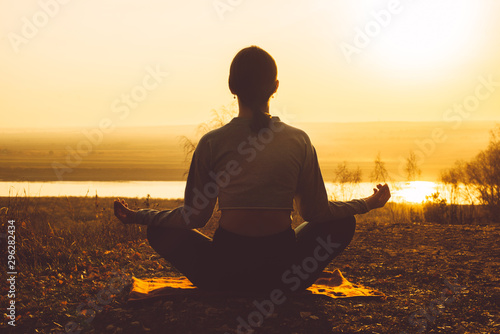 Rear view of a girl meditating in nature at sunset.