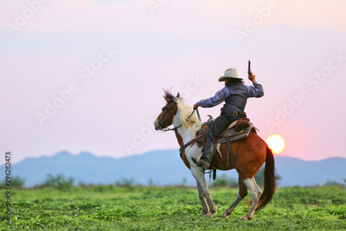Mon riding horse against sunset with holding gun © FotoArtist