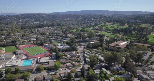 Aerial of houses in suburbs with college football ground and lush green golfing ground on a sunny day with clear blue sky and mountains in the background photo