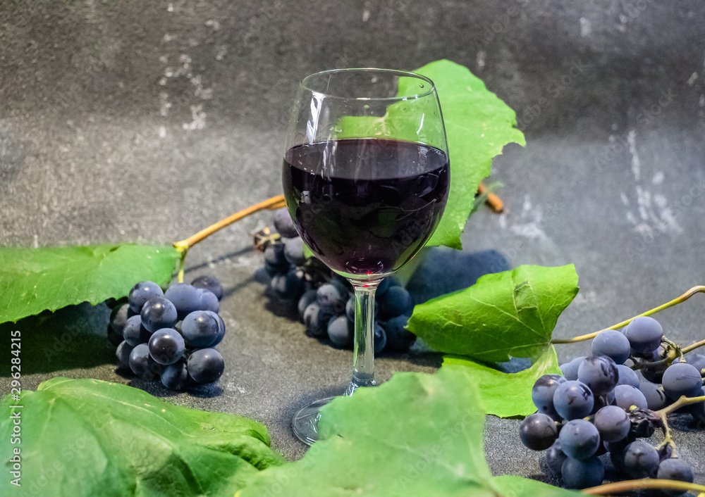 Grapes in a glass with wine on a black background. Grones of grapes with green leaves..