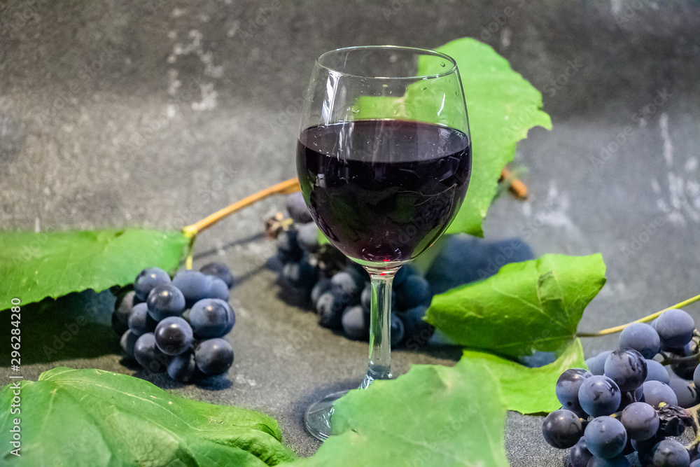 Grapes in a glass with wine on a black background. Grones of grapes with green leaves.. Grapes in a glass with wine on a black background. Grones of grapes with green leaves..