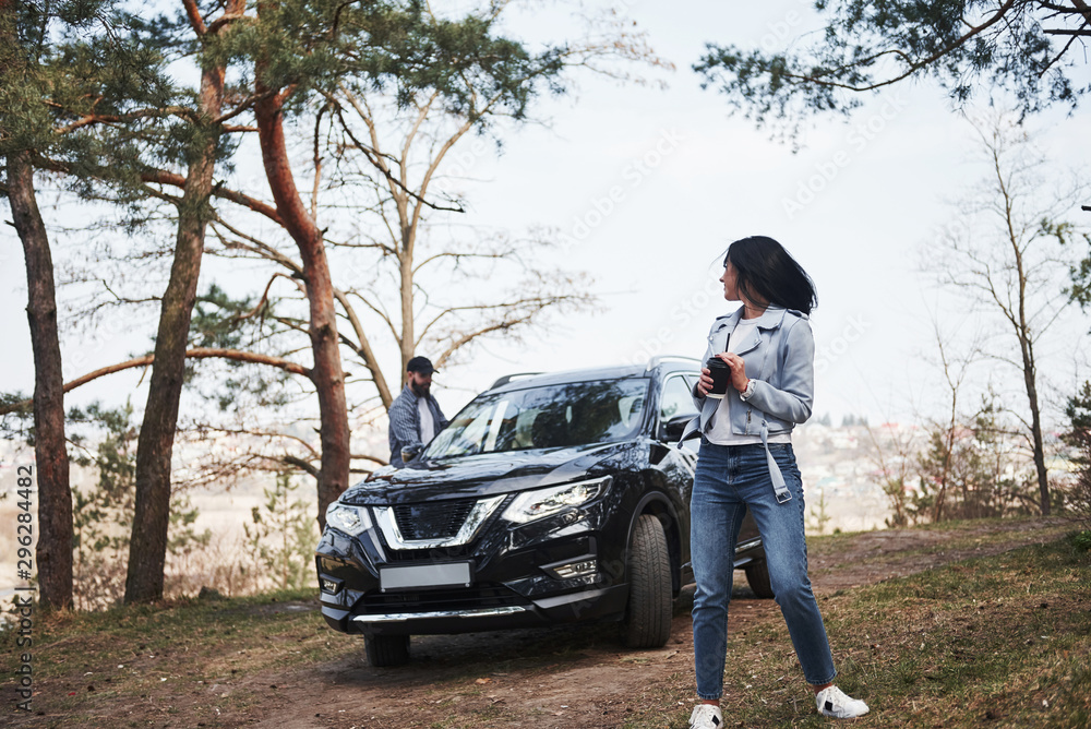Looks behind at boyfriend. Couple have arrived to the forest on their brand new black car Looks behind at boyfriend. Couple have arrived to the forest on their brand new black car